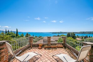 Eine Terrasse mit zwei weißen Stühlen, einer Ziegelwand und Blick auf einen See.