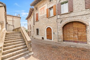 A narrow cobblestone street with a stone staircase leading up to a building with a large wooden door and arched windows.