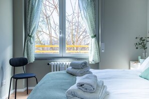 A bedroom with a bed, a chair, a radiator, and a window with curtains.