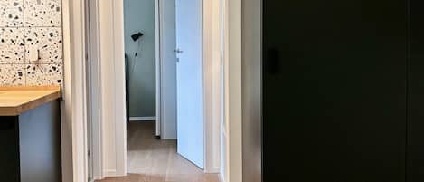 Ein Flur mit Holzboden, weißen Wänden und einer schwarzen Tür rechts.