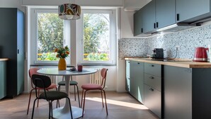 Cocina moderna con comedor, ventana con vistas a zonas verdes y un hervidor rojo en la encimera.