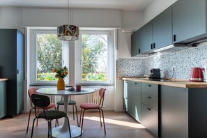 A modern kitchen with a dining area, a window with a view of greenery, and a red kettle on the counter. - Porta21 Studio [Linate, Osp.Monzino, Arena Santa Giulia] (Milano)