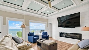 A spacious living room with a large TV, comfortable seating, a fireplace, and a view to the outside. - Experience oceanfront bliss at Magic Hour, Oak Island's spacious 7-bedroom retreat for 16. (Oak Island)
