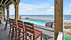 A wooden deck with a pool, chairs, and a view of the ocean. - Experience oceanfront bliss at Magic Hour, Oak Island's spacious 7-bedroom retreat for 16. (Oak Island)