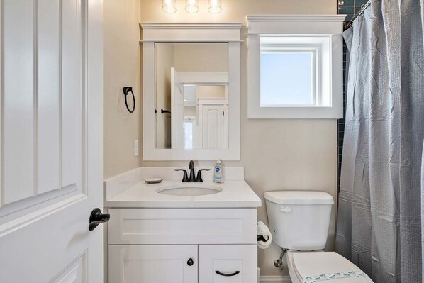 A bathroom with a white vanity, a sink, a toilet, and a shower curtain.