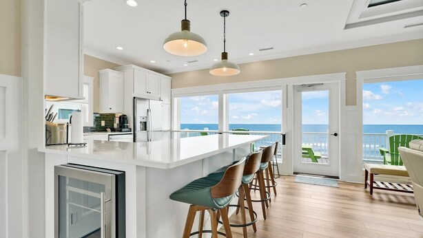 A modern kitchen with a large island, bar stools, and a view of the ocean through large windows. - Experience oceanfront bliss at Magic Hour, Oak Island's spacious 7-bedroom retreat for 16. (Oak Island)