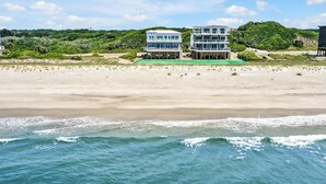 A beachfront property with a two-story building, a sandy beach, and a view of the ocean. - Experience oceanfront bliss at Magic Hour, Oak Island's spacious 7-bedroom retreat for 16. (Oak Island)