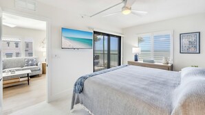 A bedroom with a bed, a ceiling fan, a window with blinds, a nightstand, and a view of the beach through the window. - UPDATED 2B/2B BEACHFRONT CONDO SEASIDE 301 (Fort Myers Beach)