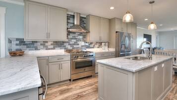 A modern kitchen with a central island, stainless steel appliances, and a herringbone tile backsplash.