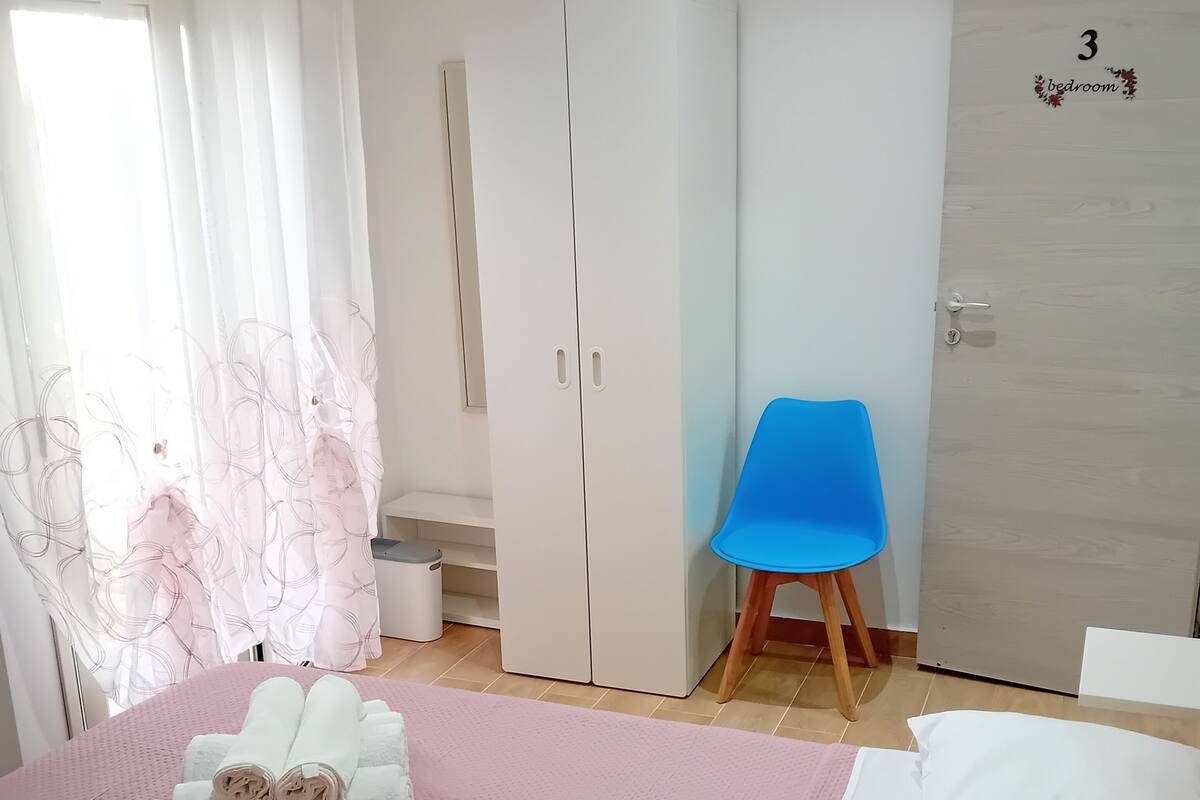 Quarto com cama, guarda-roupa, uma cadeira azul e uma porta com o número 3.