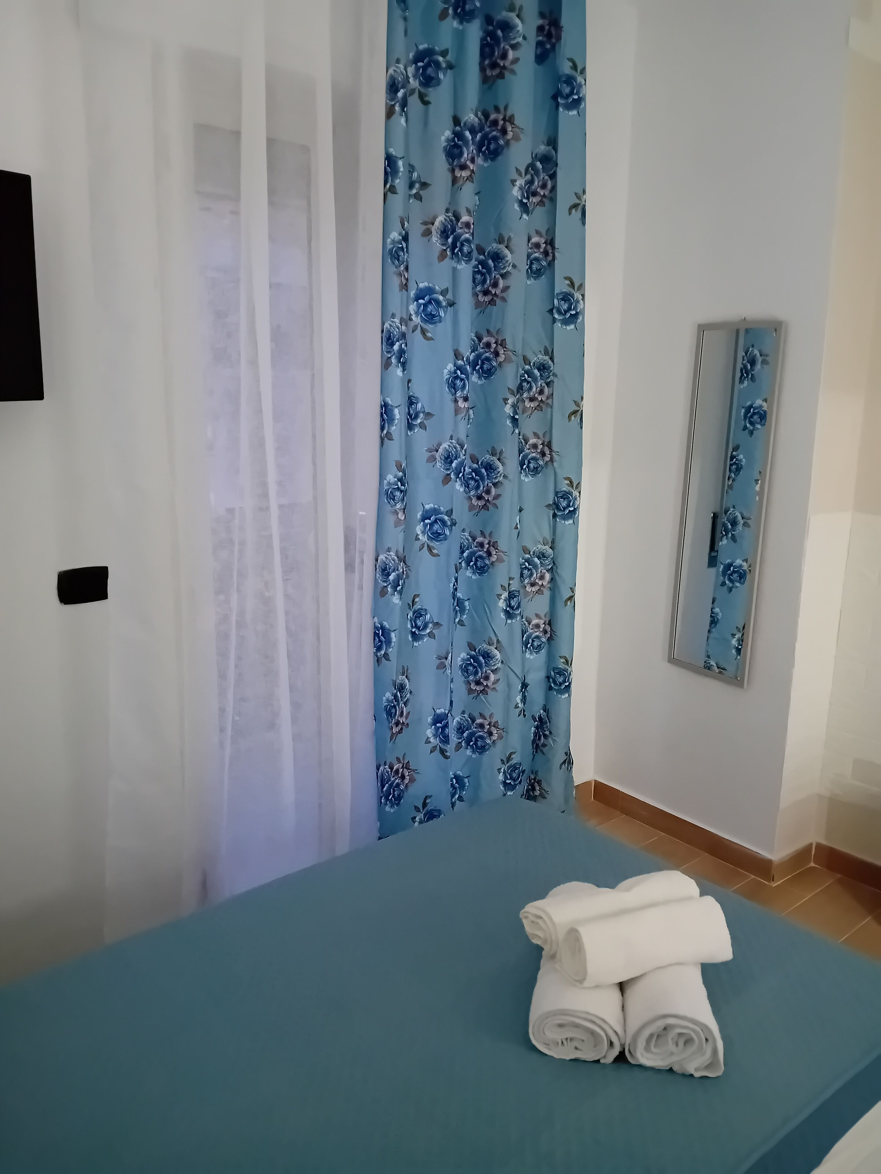 Una habitación con cama, espejo y cortina estampada con motivos florales.
