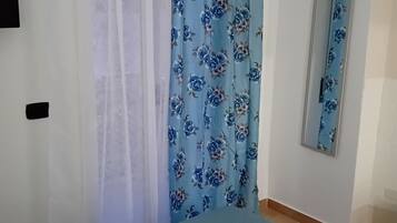 Una habitación con cama, espejo y cortina estampada con motivos florales.