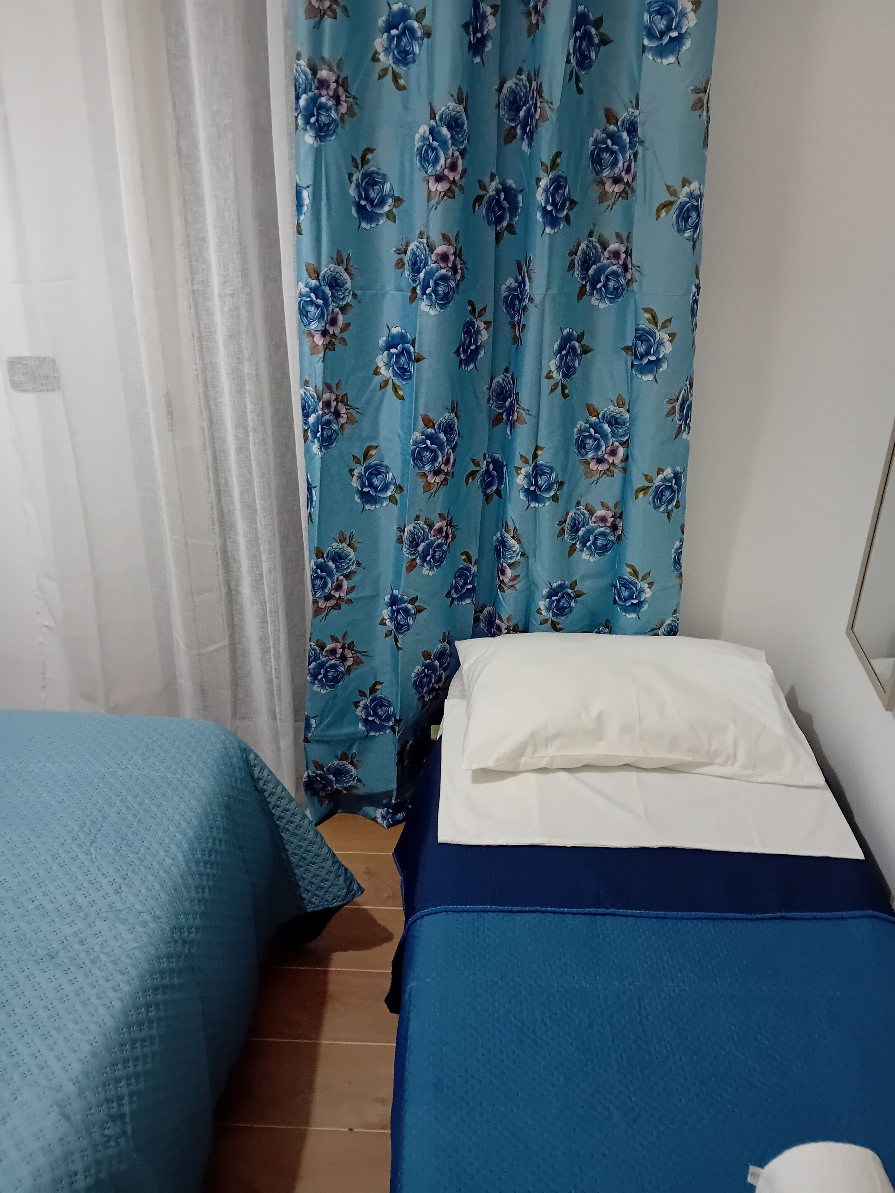 A bedroom with a bed, a pillow, a blue blanket, and a floral curtain.