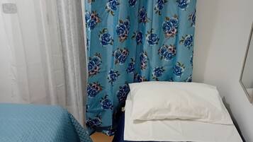 A bedroom with a bed, a pillow, a blue blanket, and a floral curtain.