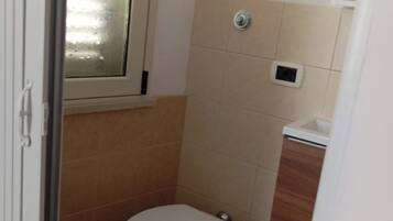 A small, compact bathroom with a toilet, a bidet, and a window.