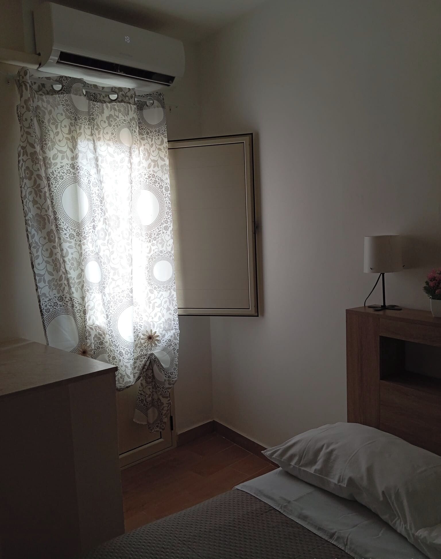 Une chambre avec un lit, une table de chevet, une lampe et un climatiseur fixé au mur.