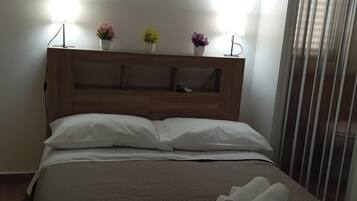 Hotelkamer met houten hoofdbord, twee kunstwerken aan de muur, een bedlamp, een bed met witte lakens en een raam met zonwering.
