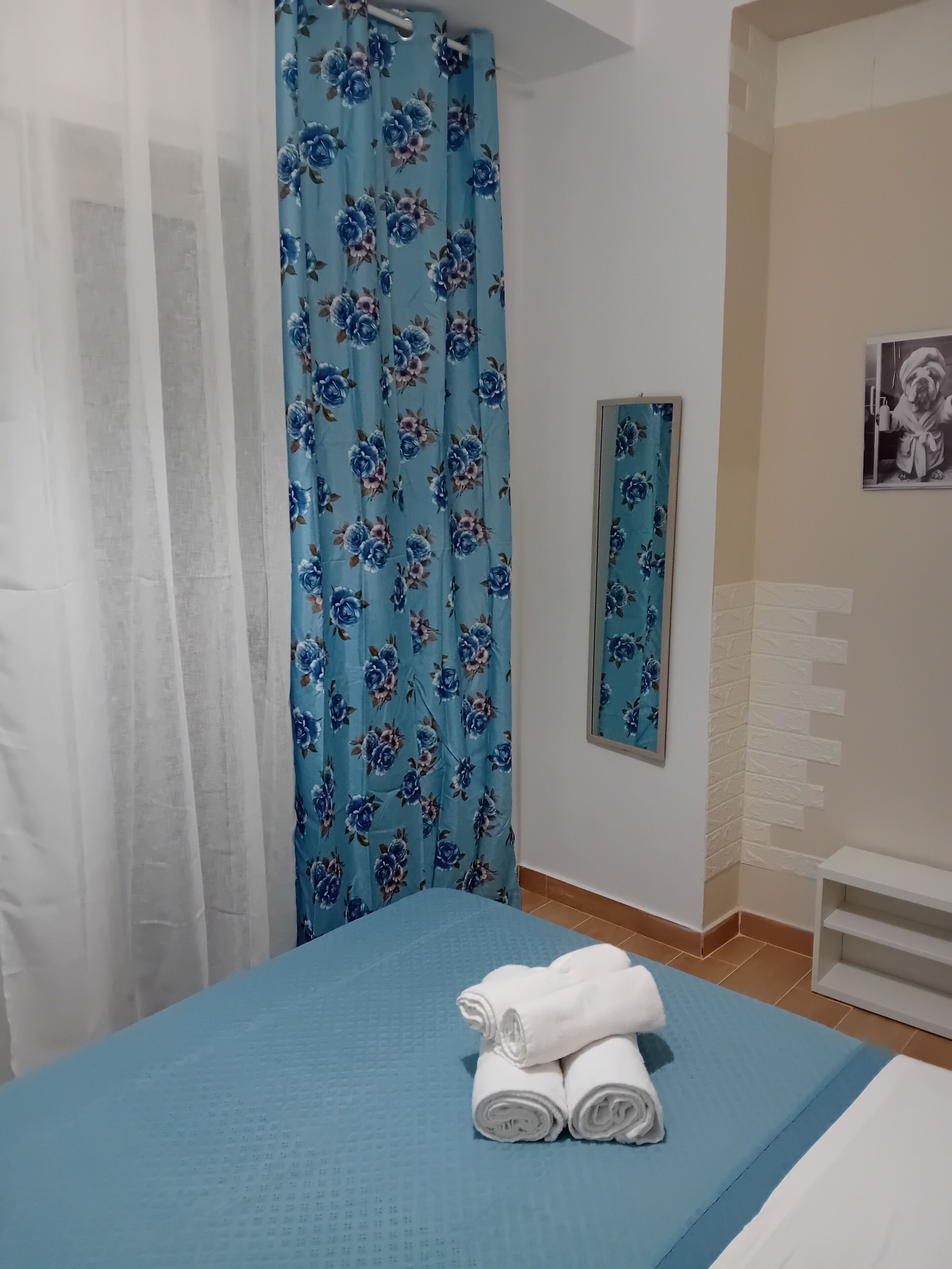 Une chambre à coucher avec un lit, un rideau à motifs floraux bleus, un miroir et une serviette blanche posée sur le lit.