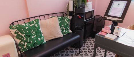 Une pièce avec un banc en métal noir, des coussins à motifs verts, un petit bureau avec un ordinateur et un sol carrelé.