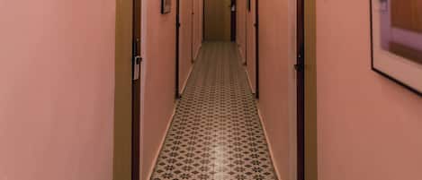 Ein Hotelgang mit rosafarbenen Wänden, nummerierten Türen und gemusterten Bodenfliesen.