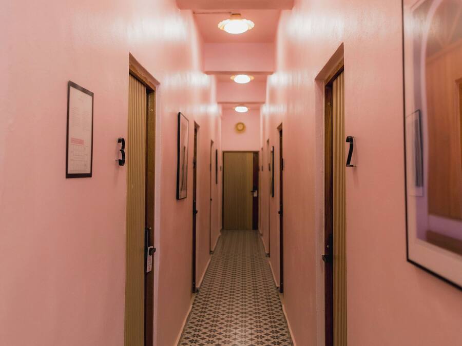 Un pasillo de hotel con paredes rosas, puertas numeradas y baldosas de suelo estampadas.