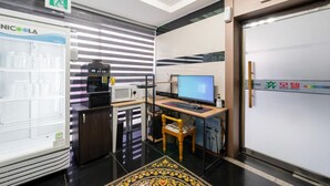 A modern hotel lobby with a refrigerator stocked with beverages, a coffee machine, a computer desk with a chair, and a reception desk. - HUE MOTEL (Gumi)