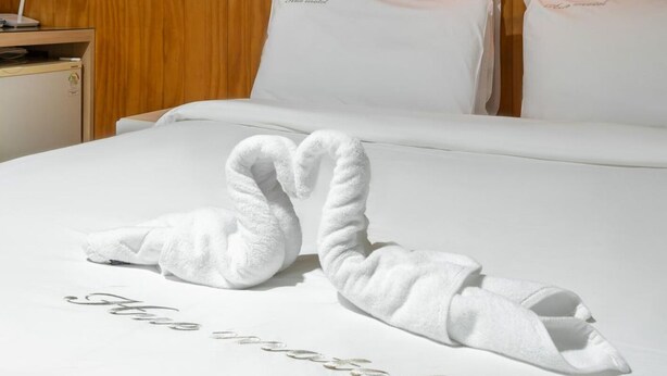 A hotel room with a neatly made bed, two pillows with the text "Nice hotel" on them, and a pair of towels arranged in a swan shape on the bed. - HUE MOTEL (Gumi)