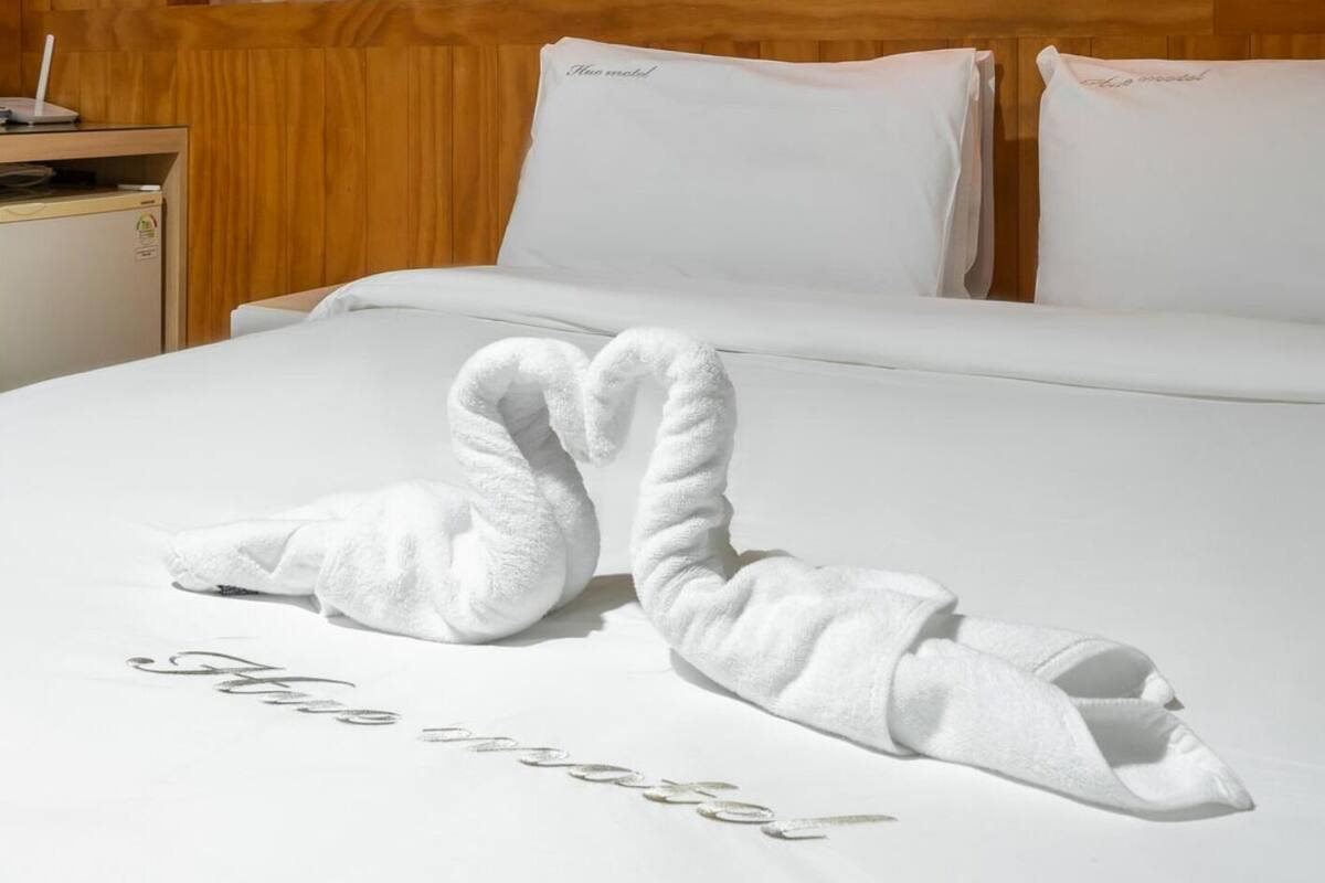 A hotel room with a neatly made bed, two pillows with the text "Nice hotel" on them, and a pair of towels arranged in a swan shape on the bed.