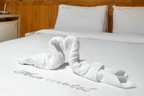 Habitación de hotel con una cama bien hecha, dos almohadas con el texto 'Nice hotel' y una pareja de toallas dispuestas en forma de cisne sobre la cama.