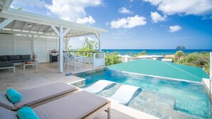 Ein Poolbereich mit Liegestühlen, einer überdachten Sitzgelegenheit und Blick auf den Ozean.