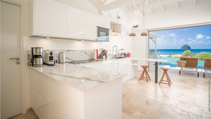A modern kitchen with a large island, white cabinetry, and a view of the ocean. - Houat (Le Diamant)
