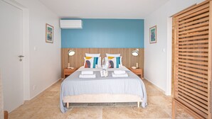 A bedroom with a bed, two bedside tables, a wooden headboard, an air conditioning unit, and a wooden wardrobe. - Houat (Le Diamant)