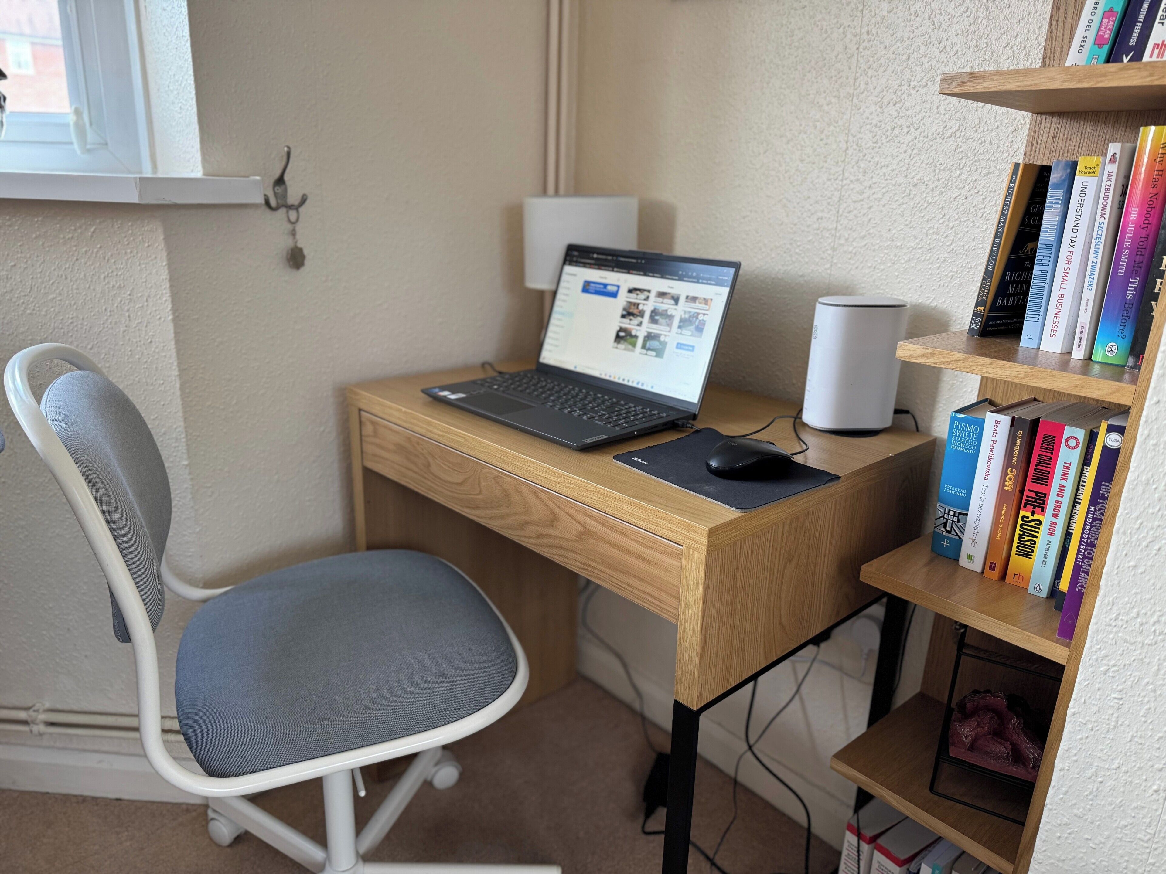 A wooden desk with a laptop, a mouse, and a bookshelf with books.