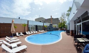 Relax by the pool surrounded by lounge chairs and umbrellas, with a view of the surrounding landscape from the adjacent building.