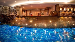 Et receptionområde med et design i træ, der er inspireret af skibe, en receptionsdisk og en pool med krystalklart, blåt vand.