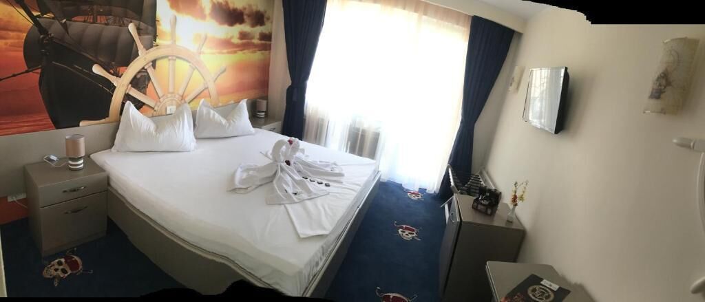 Ein Hotelzimmer mit einem Bett, einem Schreibtisch, einem Stuhl, einem Fernseher und einem Fenster mit Vorhängen.
