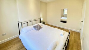 A bedroom with a single bed, a bedside table, a nightstand, and a mirror on the wall. - Lovely Two Bed Apartment In London (South Croydon)