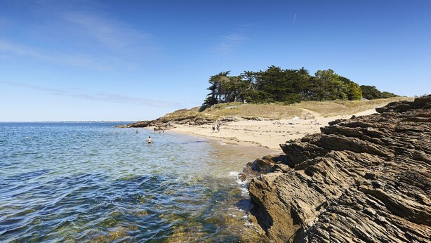 A beach with clear water, rocky shoreline, and a few people in the distance.