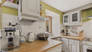 A kitchen with white cabinets, a wooden countertop, a coffee maker, a kettle, a stove, and a dishwasher.