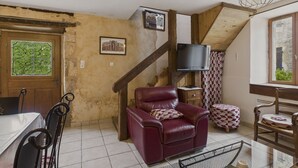 A cozy living room with a wooden staircase, a leather armchair, a TV, and a window with a view.