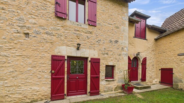 A stone building with red shutters and a small garden area.