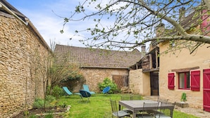 A stone house with a garden, a table with chairs, and a blue chair.
