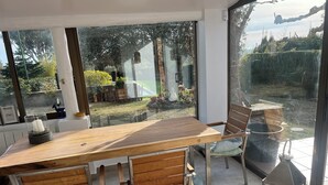 Un comedor moderno con una mesa y sillas de madera, un espacio acristalado con una vela, y vista a un jardín a través de amplias ventanas.