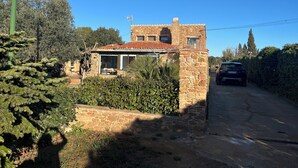 Una casa de piedra con techo de tejas, un coche estacionado adelante y un camino de tierra que la lleva.