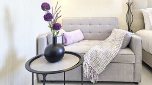 Una sala de estar moderna con un sofá gris, una mesita redonda negra y un jarrón con flores moradas.