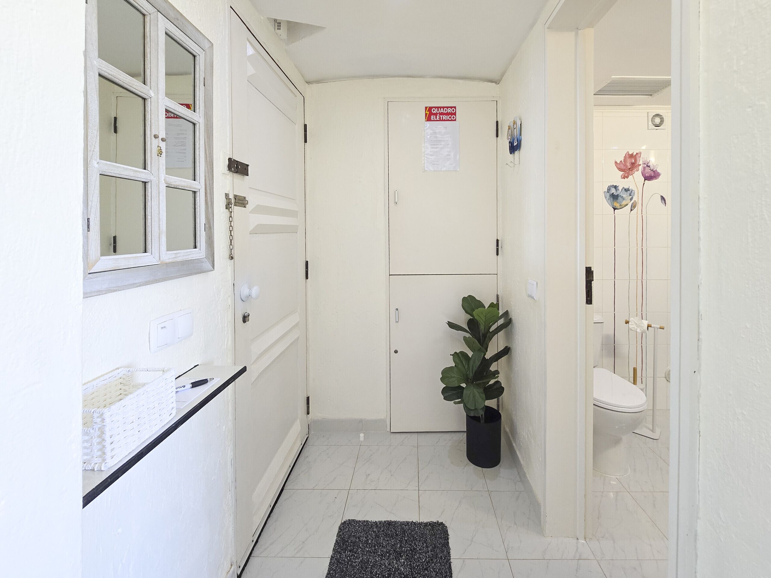 A narrow hallway with a white door, a window, and a potted plant.