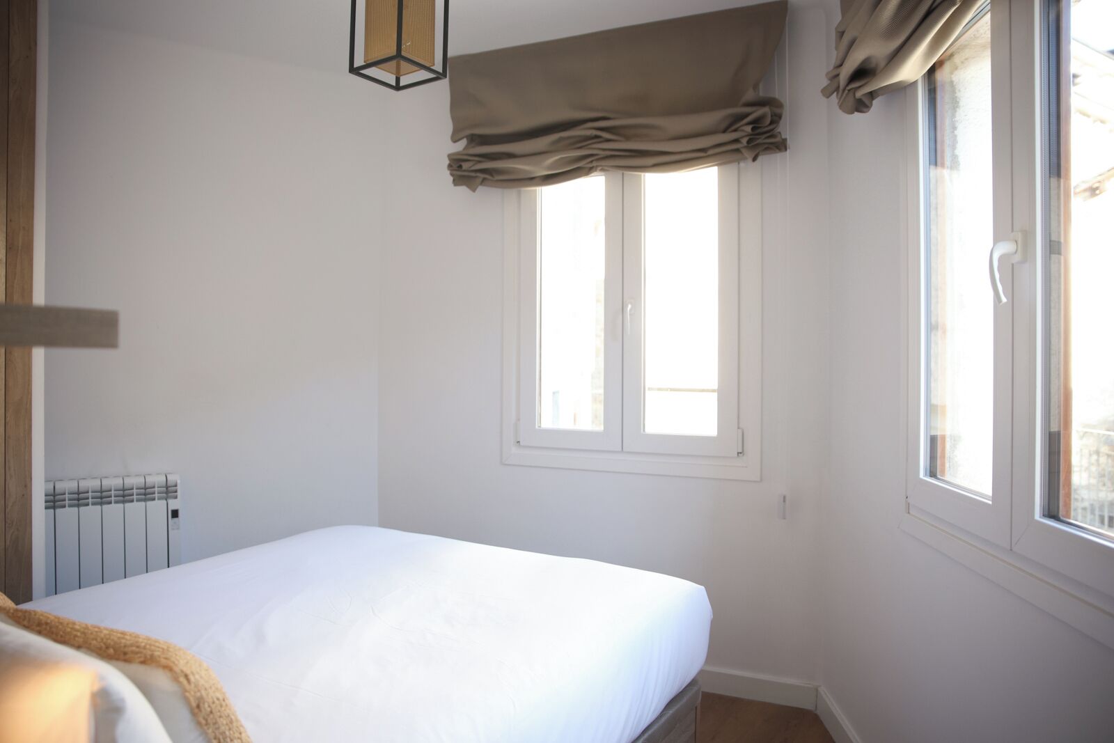 Un dormitorio con una cama individual, un radiador, una ventana con cortinas y una lámpara colgante.