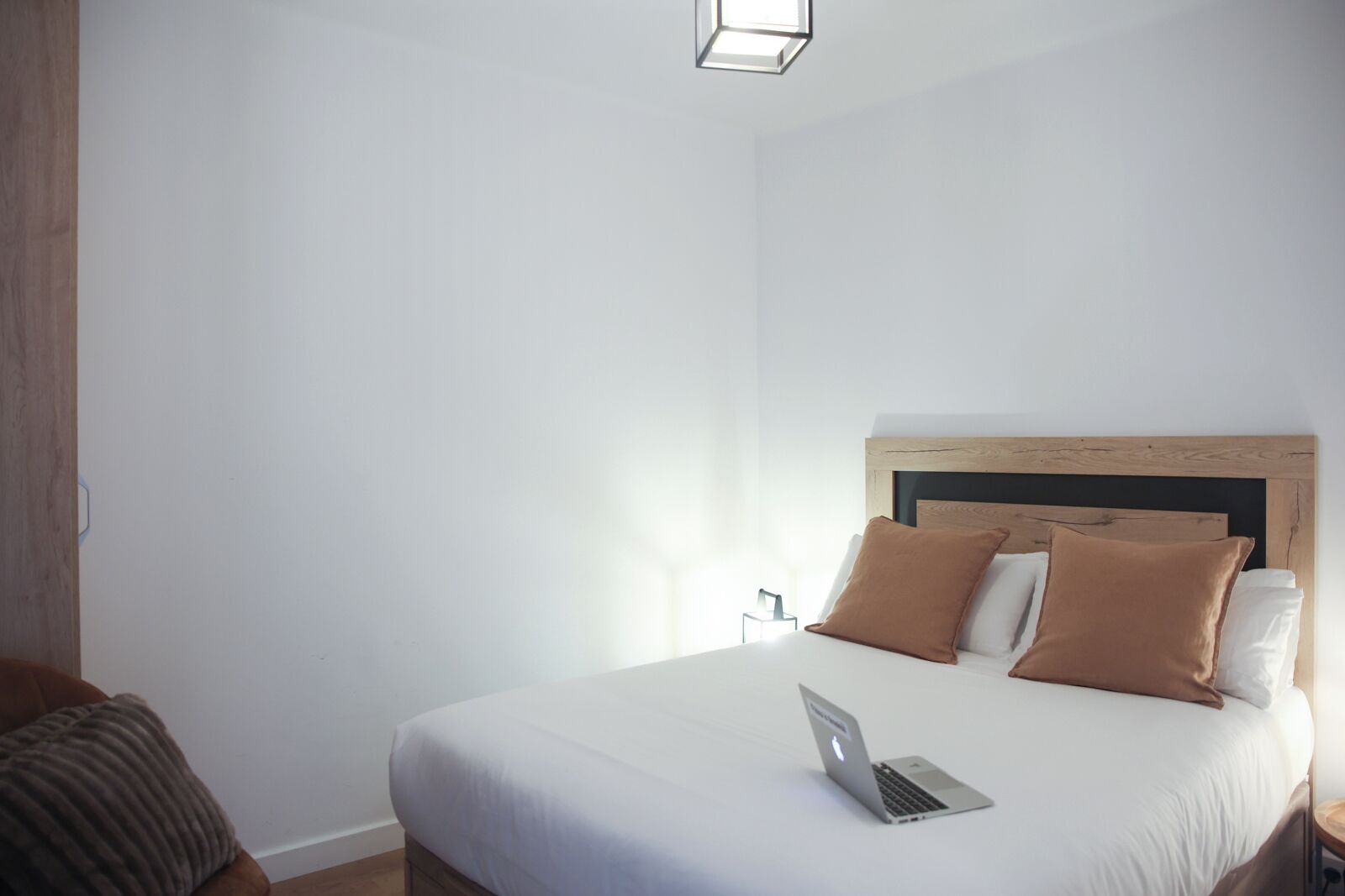 Ein ordentlich bezogenes Bett mit einem Laptop darauf, einem Holzkopfteil und einem Nachttisch mit einer Lampe.