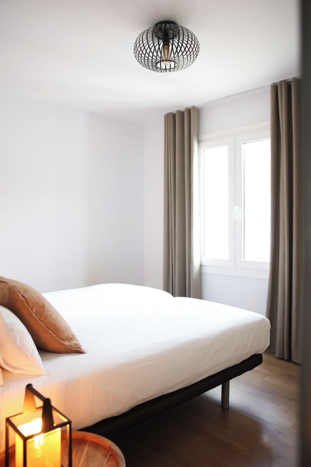Un dormitorio moderno con cama, mesita de noche con lámpara, ventana con cortinas y una lámpara de techo original.