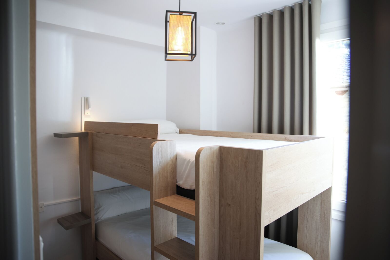 Un lit superposé avec une structure en bois et un lit simple en haut. Un luminaire suspendu se trouve au-dessus du lit.